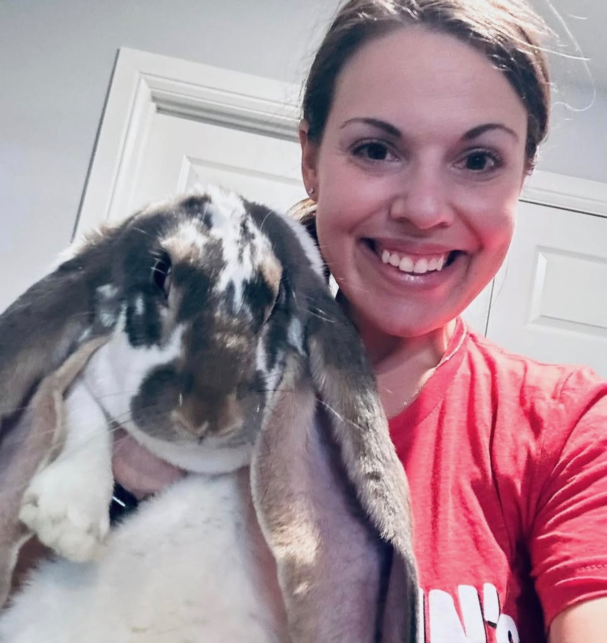 A volunteer smiling while holding a large lop-eared rabbit